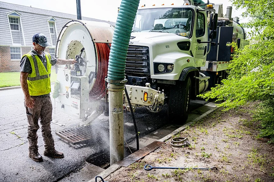 A technician operating a vacuum jetting truck over a drain